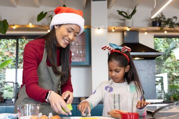 Asian mother and daughter pressing cookie cutter and baking dough in kitchen wearing aprons
