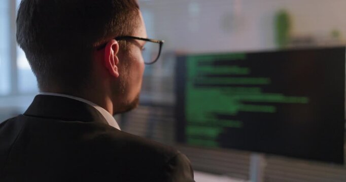 Programmer developer coder in office computer coding. Businessman engineer man reviews green code on monitor, focused at desk in corporate workspace. Concept highlights modern software development.