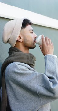 Vertical video: Adult male raising coffee cup to lips smiling while sipping for warmth on street