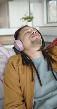 Vertical video: Pink headphones playing audio lulling African American man reclining sofa at home