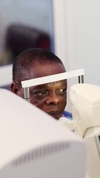 Vertical video, African patient receiving eye examination with a non-contact tonometer (NCT) equipment for vision health