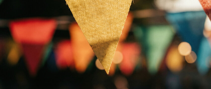 A close-up of a string of colorful bunting flags with bokeh lights in the background