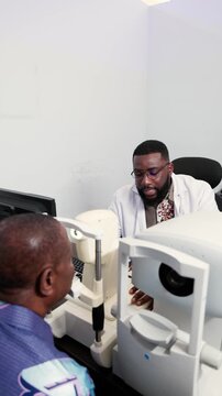 Vertical video, Optometrist examining a senior African man's eyes in a clinic with a non-contact tonometer (NCT)
