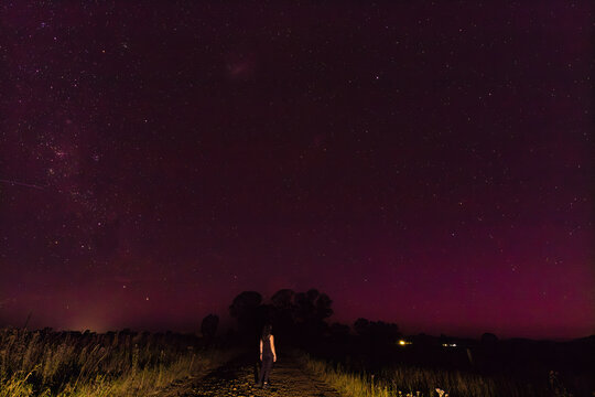 Woman standing on country road under starlit sky with faint Aurora Australis