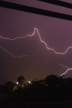 Lightning forks illuminating the night sky outside a bedroom window