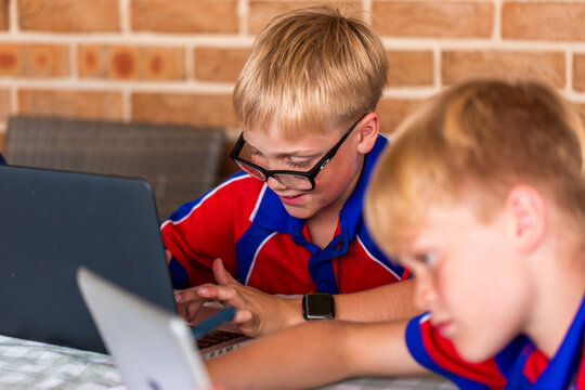 School children using tech devices for homework at outdoor table at home