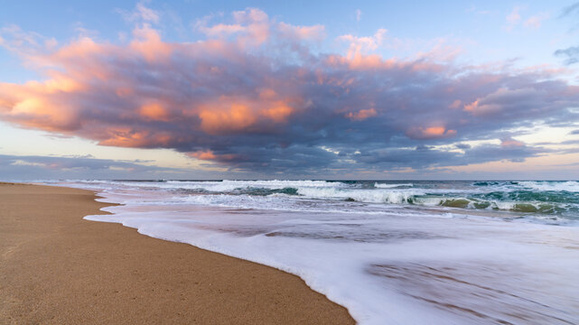 Low angled view of a colourful storm clouds over waves breaking in a sandy beach at twilight
