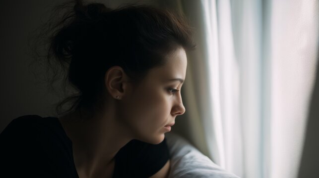 Retrato de perfil de mujer joven con expresi&oacute;n seria o pensativa mirando a trav&eacute;s de una ventana con luz suave, tristeza por alguien que se va