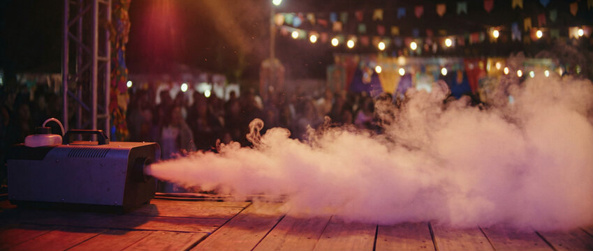 A fog machine emitting smoke on a stage with a crowd in the background