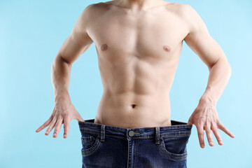 Athletic man wearing big jeans on light blue background, closeup