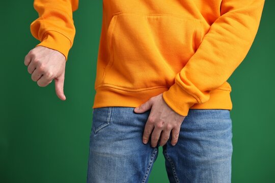 Urology. Man covering his groin with hand and showing thumbs down on green background, closeup