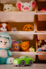 Naklejka premium Green plastic toy car on the floor in a child room. Soft plush bear and stuffed animals on the shelf in the background. Concept of childhood, fun activity and childhood creativity.