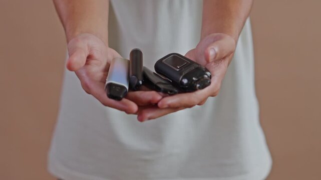 Close up of hands holding variety of electronic cigarette devices and vape pods against neutral studio background