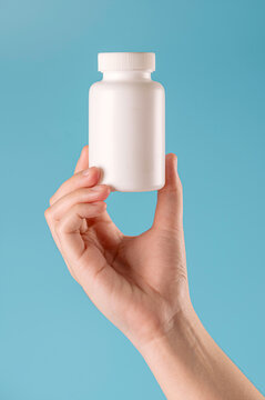Close-up of  hand holding  blank white plastic pill bottle against blue background. Ideal for medical, healthcare, vitamins, or beauty product branding and packaging mockups.