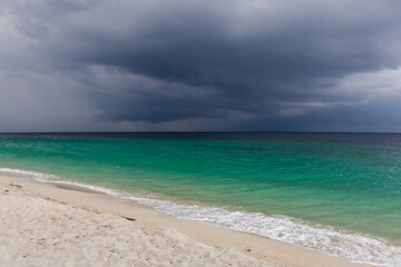 Obraz premium Koh Adang beach with dark stormy sky and turquoise ocean waves. Sand stretches along calm shore. Dramatic clouds over tropical coastline in Thailand.