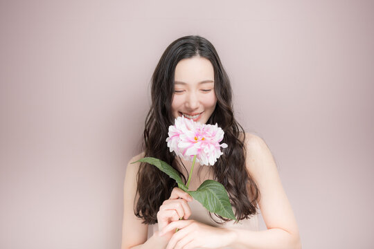 ダリアの花を持って多幸感にあふれるピンクの春色イメージの女性の美容ビューティーイメージ　ピンク背景の上半身
