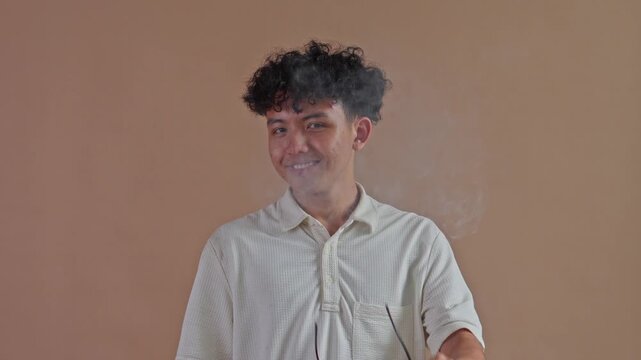 Cool male model in white polo shirt using an electronic cigarette and blowing smoke clouds