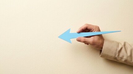 arrow blue hand point direction left business concept showing the way forward with a minimal blue arrow sign held by a male hand against a neutral beige wall copy space