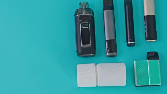 Flat lay of various electronic cigarette devices and e-liquid bottle on turquoise background