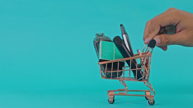 Hand pushing mini shopping cart filled with vape devices isolated on turquoise background