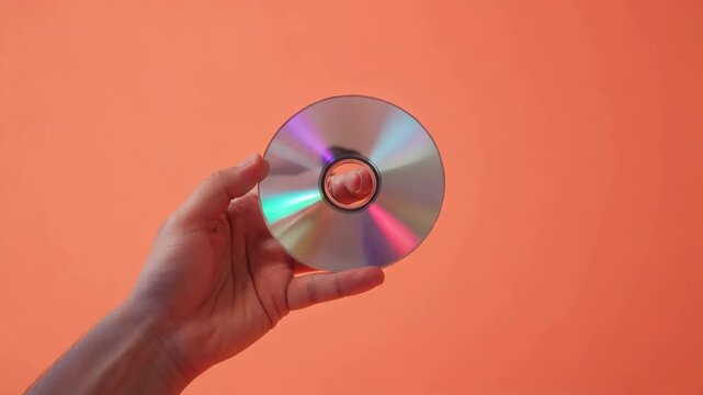 コーラル背景で光沢CDを指に通して見せる手のミニマル写真