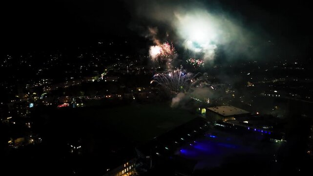Night-time aerial drone footage of a colourful fireworks display exploding over the city of Bath England with urban city lights in the background during a celebration