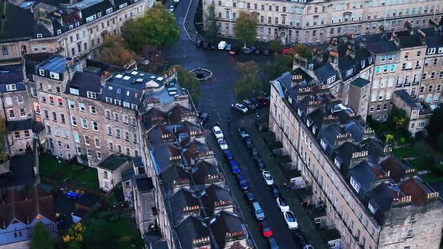 High angle aerial drone footage of a historic residential area in Bath, Somerset. The shot features classic honey-colored Georgian architecture, slate roofs, and chimney stacks overlooking wet streets
