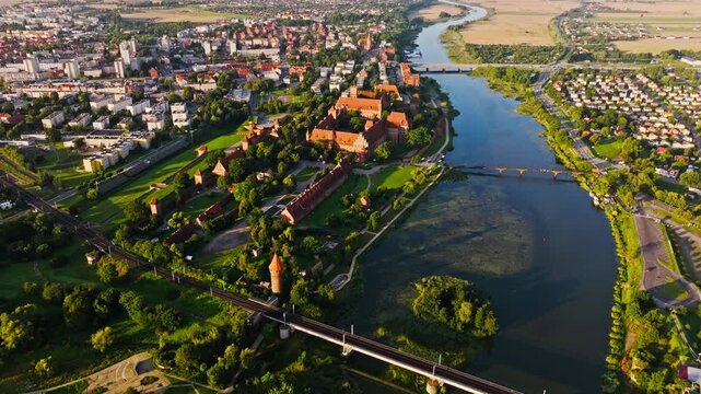Cinematic drone flight shows Malbork Castle emerging through calm early sunrise
