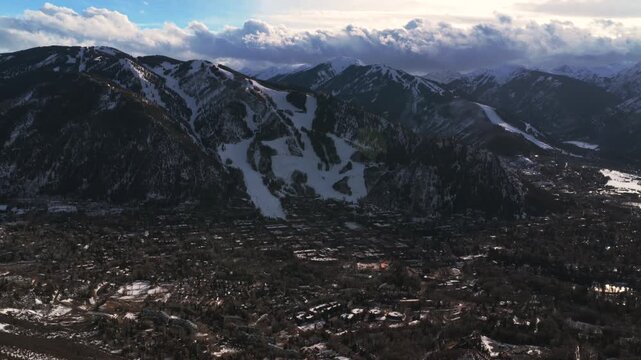 Aspen Mountain downtown ski town cloudy sunset AJAX Aspen Highlands Ski resort aerial drone Colorado ski trail runs fresh snow Rocky Mountains peaks chairlift gondola roaring fork valley pan left