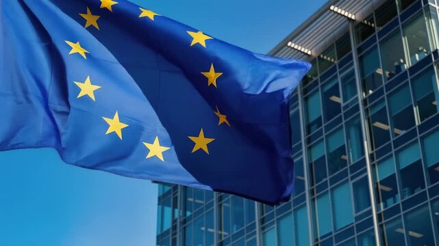 European Union flag waving outside modern glass office building on clear blue sky day