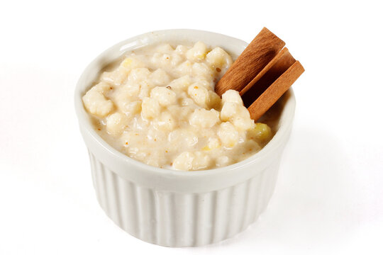 Mungunza, or Brazilian creamy canjica, served in a white ceramic ramekin and decorated with cinnamon sticks, isolated on a white background