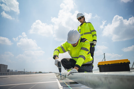 Professional technician using electric drill for solar panel installation on rooftop with sunny sky background, Engineer installing photovoltaic system for sustainable green energy and renewable power