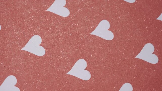 Top view of rotating white hearts pattern on red textured paper background, Minimalist red paper texture with white heart shapes for holiday greeting cards