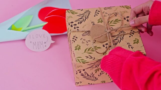 Woman's hands carefully pulling twine on decorated gift box for Mother's Day celebration