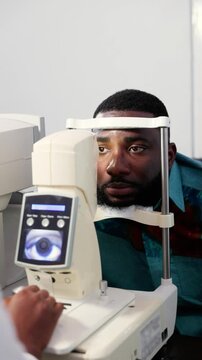 Vertical video, African female optometrist performing an eye exam for a male patient using a non-contact tonometer (NCT)