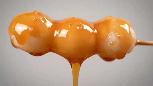 Macro shot of traditional japanese mitarashi dango glazed with thick, sticky sweet soy sauce (mitarashi sauce) dripping down the rice dumplings on a wooden skewer.