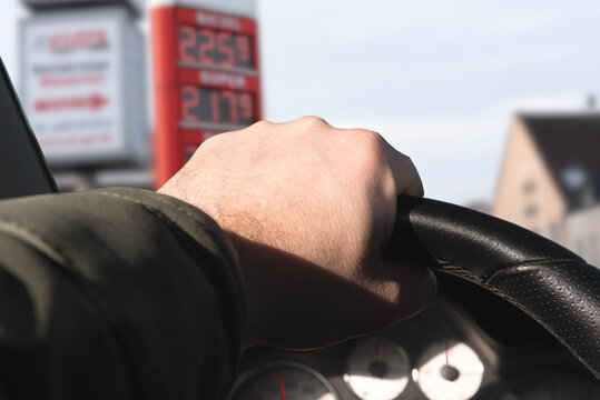 Ein Mann f&auml;hrt einen Wagen zu einer Tankstelle. Preistafel zeigt hohe Kraftstoffpreise.