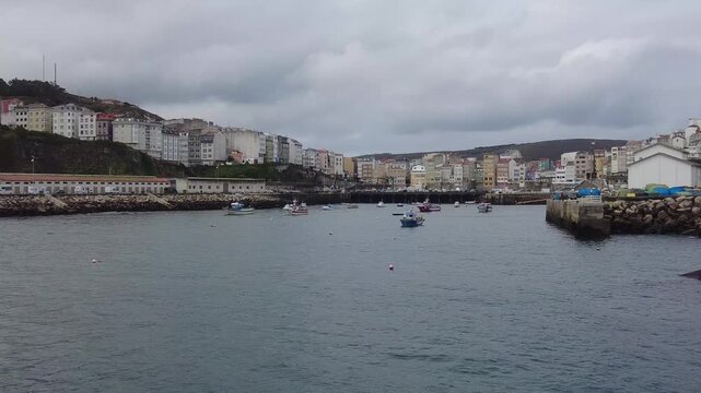 Panoramic view of the quaint fishing village of Malpica de Bergati&ntilde;os in Galicia, Spain, showing boats peacefully floating in the harbor under a dramatic cloudy sky on a serene day