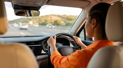 Rear view of a focused African American woman confidently driving a modern car on a busy highway during a bright. © Esther