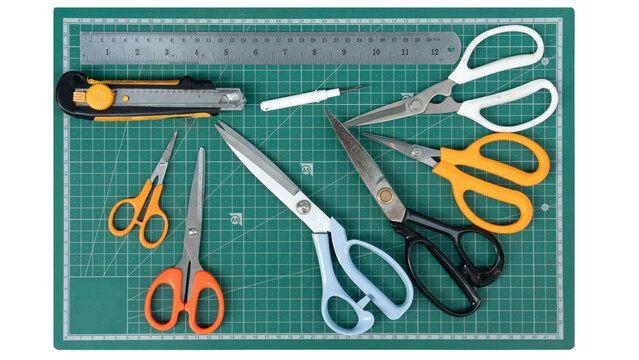 Craft tools and equipment including scissors a knife and a thread cutter. Place it on the green cutting mat. On isolated white background.