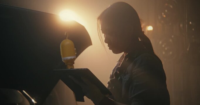 Asian Female Professional Performs Final System Sweep Using Wireless Diagnostic Tablet. Woman Seen Clearing Dashboard Warning Lights and Updating Digital Service Log With Technical Specifications.