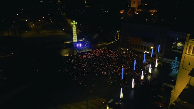 Night aerial view of torchlight march crowd at Freedom Square in Tallinn during Estonian Independence Day beside the illuminated Freedom Cross monument.