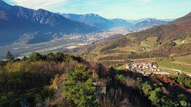 Drone flight over Adige Valley in autumn. Reveals historical ruins, the turquoise river, Valsorda village with vineyards, and the city of Trento framed by the Alps