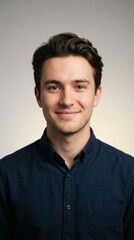 Obraz premium Young man smiling for professional headshot in studio setting, wearing casual navy blue shirt for corporate social media profile and business recruitment advertisement