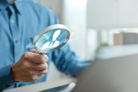 Business professional holding magnifying glass with employee icon, symbolizing recruitment, candidate selection and talent acquisition. Concept of human resources management and hiring process.