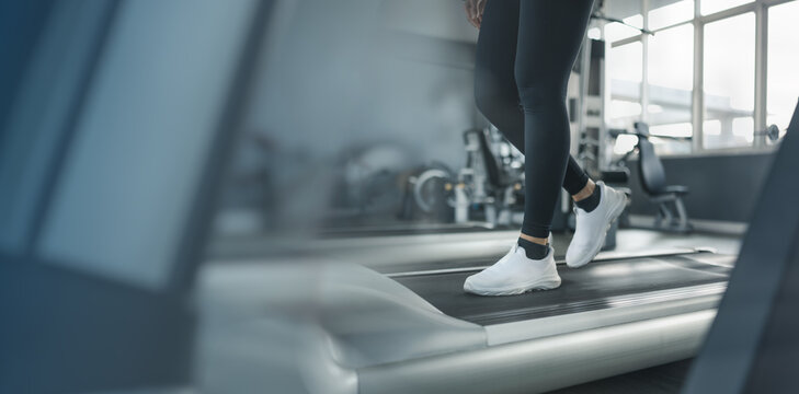 Close up of woman walking on treadmill in modern gym with copy space, representing fitness background and healthy lifestyle concept. Focus on cardio training, endurance and active living.