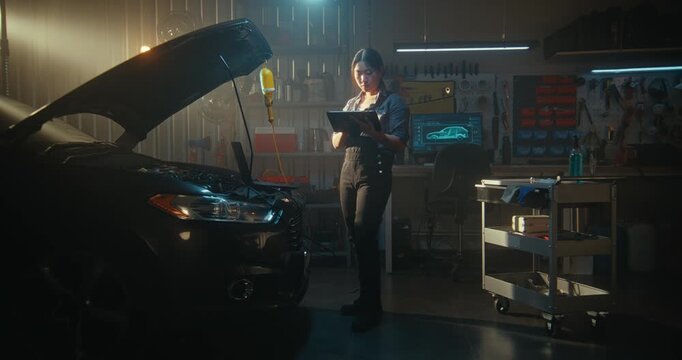 In Garage Woman Technician Combining Traditional Mechanics With Digital Innovation. Female Analyzes Vehicle Diagnostics on Laptop While Consulting AI Assistant Via Tablet For Precise Troubleshooting.