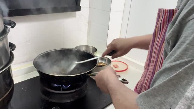 Cooking food in a wok at home kitchen, with pieces of battered ingredients deep frying in hot oil while being stirred with a metal spatula, showcasing energetic Chinese home cooking in Xi'an, China.