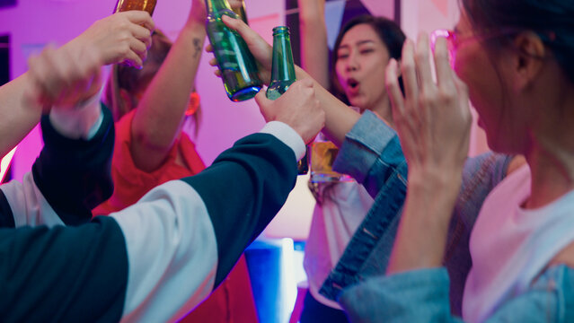 Closeup hands multiethnic young adult Asia friend wear futuristic neon glowing glasses dance and drink alcohol beer fun hangout party in living room night indoor home. Disco lights illuminating house.