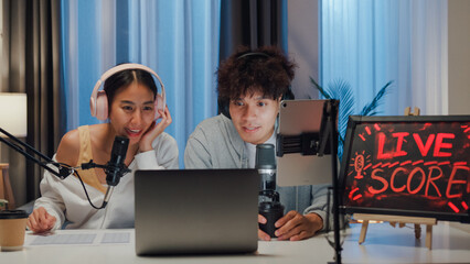 Young happy Asian couple wear headphone sit on desk online live streaming football live score...